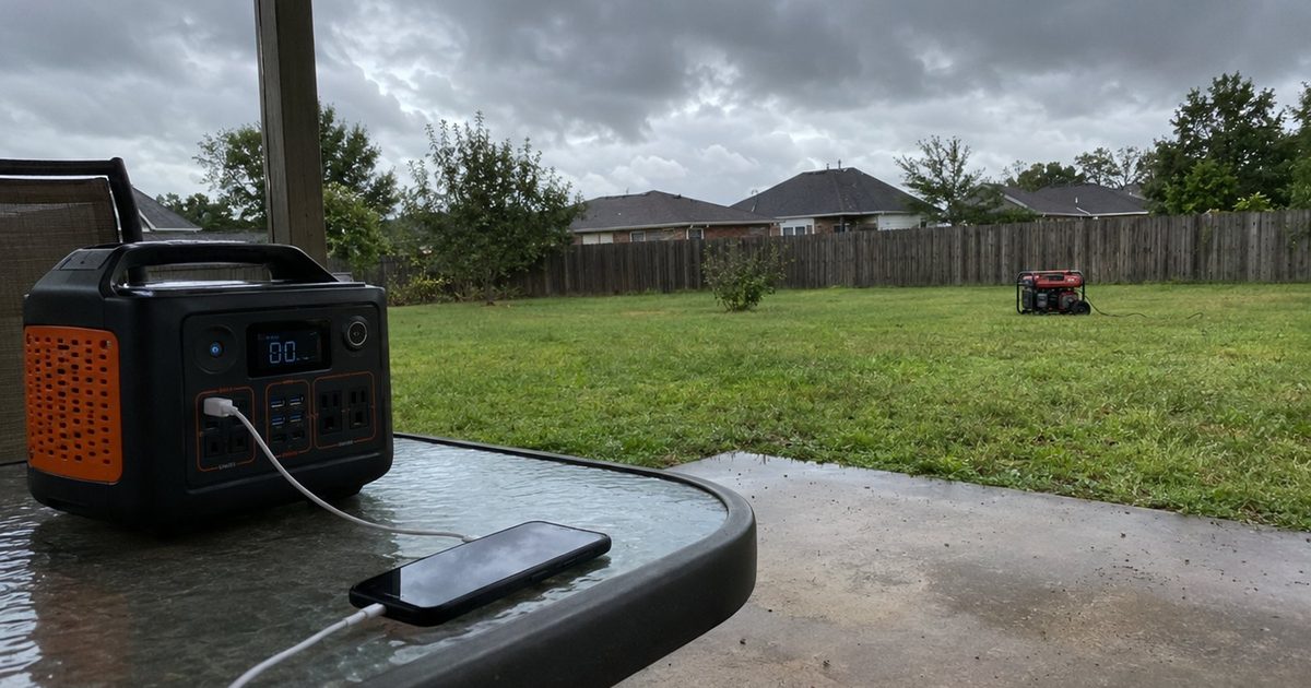 A portable power station on a porch beside a gas generator sitting safely out in the yard